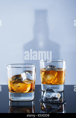 Two glasses of whisky and ice on a light background with a shadow from a bottle Stock Photo