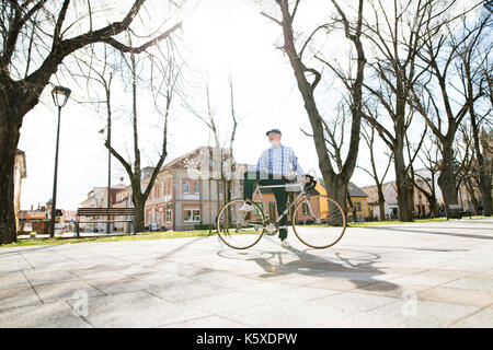 Senior man in blue checked shirt with bicycle in town. Stock Photo