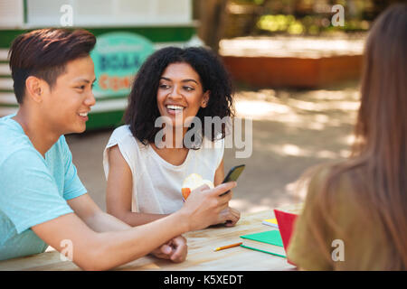 Side view of happy three friends sitting by the table outdoors Stock Photo