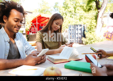 Side view of friends sitting by the table outdoors and using their smartphones Stock Photo