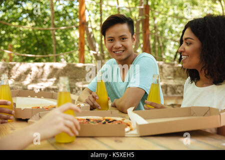 Friends sitting by the table in forest with drinks and pizza Stock Photo