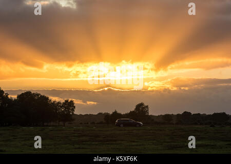 A car passing in front of an autumn sunset at Bramble Hill on the New Forest, Hampshire, UK. Stock Photo