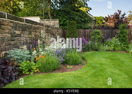 Corner of beautiful, private, traditional, landscaped, country garden, Yorkshire, England, UK - summer flowering plants bloom on herbaceous border. Stock Photo