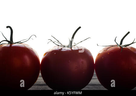 Three Red Tomatoes Standing in a Row on a Black Wooden Table Against White Background Close-Up. Silhouette of Tomatoes concept Stock Photo