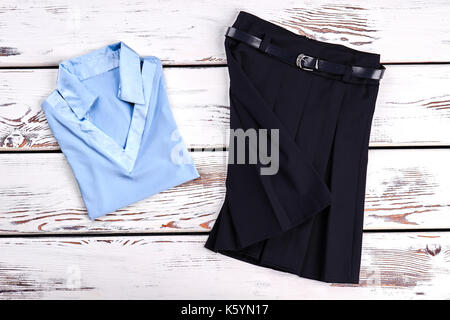Beautiful set of school clothes for girl. New light blue girls blouse and black pleated skirt for school wear, old wooden background. Stock Photo