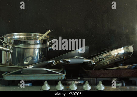 An horizontal image of a pile of dirty pans stacked on a greasy gas stove top in front of a black background. Stock Photo