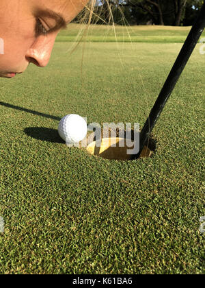 Young Female Golfer Blowing Golfball Into Hole Stock Photo