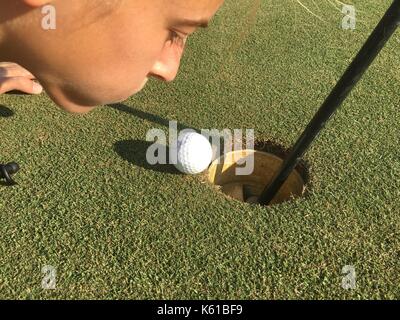 Young Female Golfer Blowing Golfball Into Hole Stock Photo
