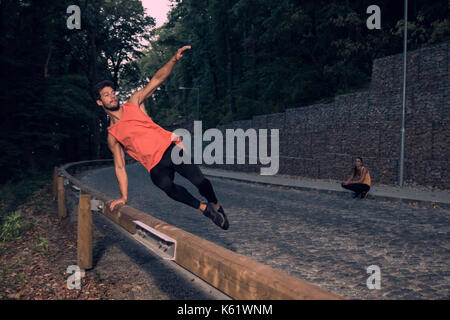 two young people, adventure, road forest outdoors, man jumping fence parkour, street stunt, rural area, woman background behind, jump in air Stock Photo