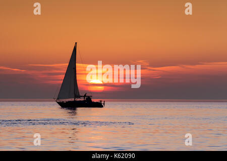 A person setting sail on a yacht as the sun sets over the horizon of cardigan bay Stock Photo