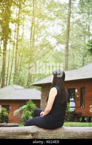 Girl sitting on wooden bench outside in a green park looking at