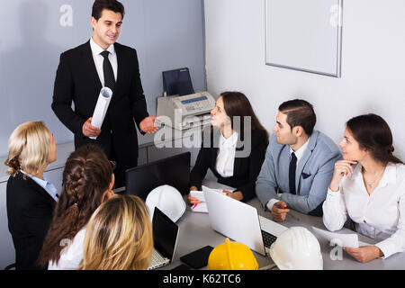 Team of smiling engineers discussing business project in office interior. Focus on sitting man Stock Photo