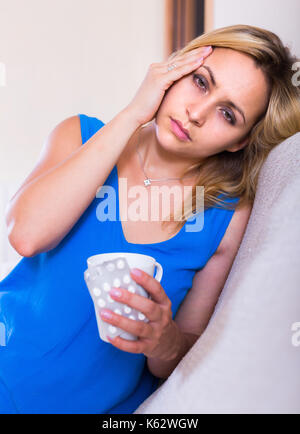 Portrait of young blonde woman suffering from headache at home Stock Photo
