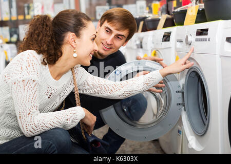 Young couple choosing washing machine in supermarket and smiling Stock Photo