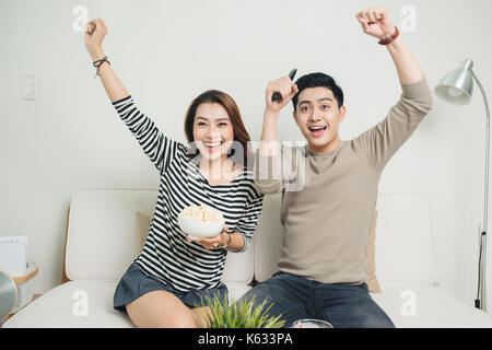 Excited young asian couple watching TV and eating popcorn Stock Photo