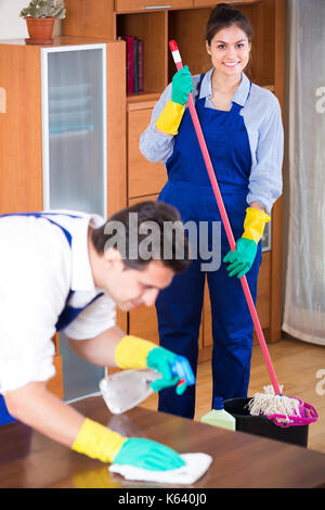 Two positive professional cleaners cleaning and dusting in ordinary apartment Stock Photo