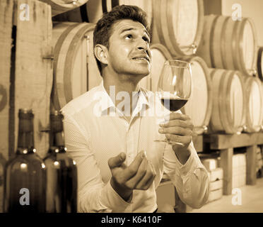 positive adult man having bordeaux wine tasting in cellar with woods ...