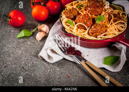 Spaghetti pasta with meatballs, basil tomato sauce in red cast iron pan, on black stone table copy space Stock Photo