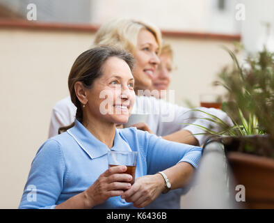 Three positive smiling mature women drinking tea at balcony. Focus on brunette Stock Photo