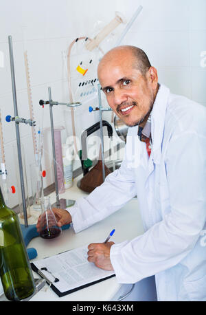 Attentive diligent smiling mature man working on quality of products in winery lab Stock Photo