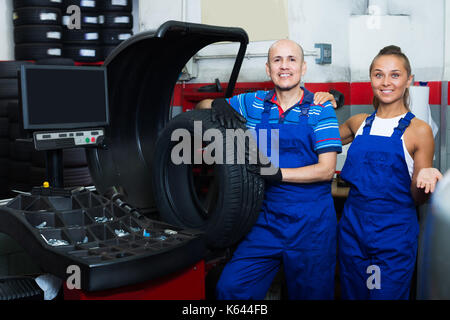 Two glad technicians working on wheel balancing machinery in car service Stock Photo