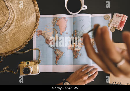 Woman planning her trip. Human hands on the world map with the hat, film camera, some money, notebook from recycled paper and freshly brewed coffee Stock Photo