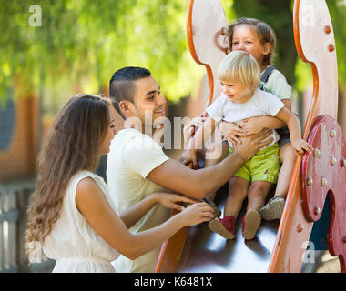 Positive happy family of four at children's playground in park Stock Photo