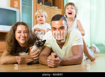 Family portrait of parents and two daughters lying on the floor at home with Siamese. Focus on man Stock Photo