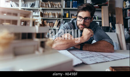 Architect looking at house model and thinking. Creative designer sitting in office and working on new project. Stock Photo