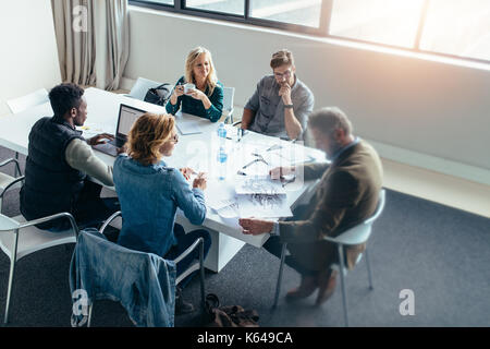 Business people working and discussing together in meeting at office. Businessman looking at building sketch with colleagues sitting around table. Stock Photo