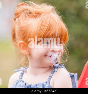 A MODEL RELEASED 2 year old girl with ginger hair and a dummy outdoors in the Uk Stock Photo