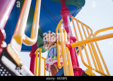 A toddler girl plays on playground equipment on a sunny day. Stock Photo