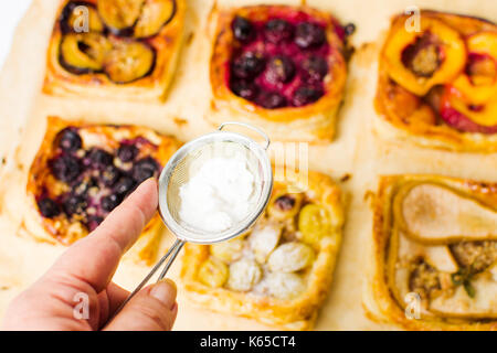 Adding sugar to fruit sweet pie slices on baking paper Stock Photo
