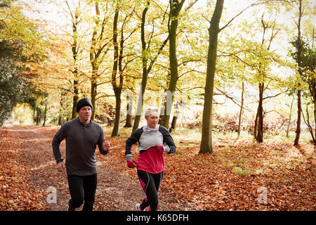 Mature Couple Running Through Autumn Woodland Together Stock Photo