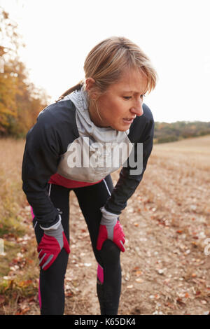 Mature Female Runner Pausing For Breath During Exercise In Woods