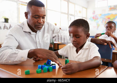 Teacher helping elementary school boy counting with blocks Stock Photo