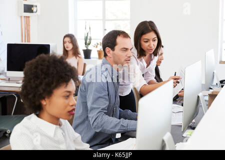 Colleagues talking at work in a busy open plan office, close up Stock Photo