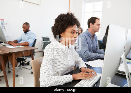Young woman at computer with colleagues in open plan office Stock Photo