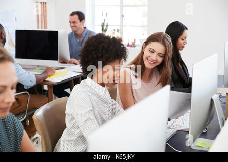 Two happy women discuss work at computer in open plan office Stock Photo