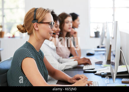 Woman with headset at computer in office beside colleagues Stock Photo