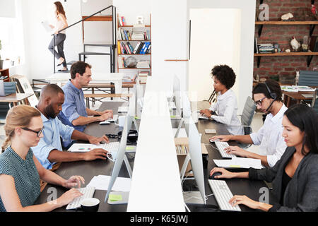 Colleagues sit using computers in a busy open plan office Stock Photo