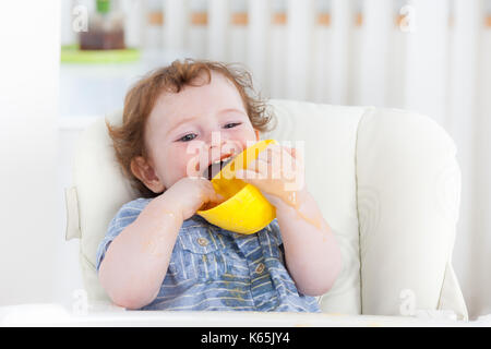 Cute baby boy eating by himself on high chair Stock Photo