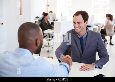 Two men sit and shake hands at a meeting in an office Stock Photo