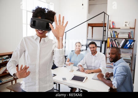 Woman wearing VR goggles watched by colleagues in an office Stock Photo