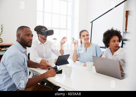 Man in VR goggles at a desk with colleagues in an office Stock Photo