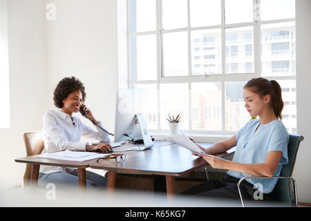 Two young women at work, on the phone and reading documents Stock Photo