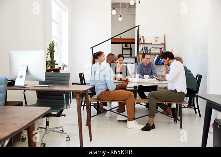 Creative team meet at a table in an office, one using phone Stock Photo