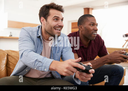 Two Male Friends Sitting On Sofa In Lounge Playing Video Game Stock Photo