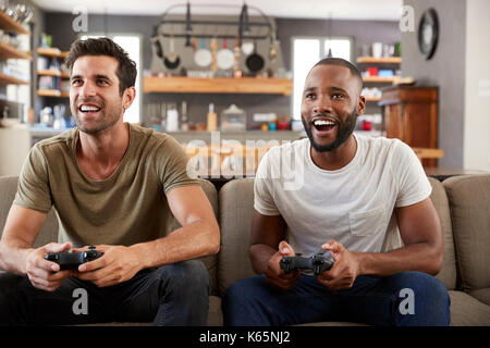 Two Male Friends Sitting On Sofa In Lounge Playing Video Game Stock Photo