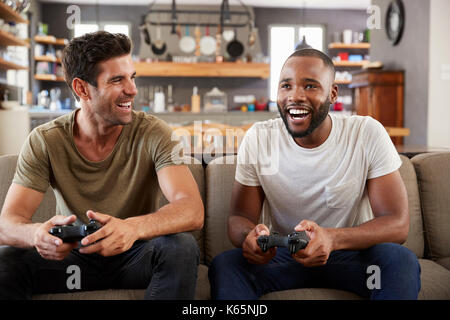 Two Male Friends Sitting On Sofa In Lounge Playing Video Game Stock Photo